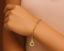 Gold bracelet with a avocado pendant/ charm on a wrist.
