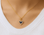 Gold necklace with a heart-shaped pendant/ charm featuring a blue gemstone & diamonds on a white background.