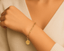 Gold chain bracelet with a gold daisy charm on a wrist against a neutral background