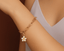 Gold chain bracelet with a flower charm on a wrist against a neutral background