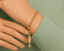 Gold bracelet with a firecracker charm on a wrist against a green background