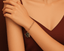 Gold bracelet with a graduation cap charm on a wrist against a brown background