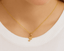 Gold necklace with 'F' pendant/ charm on a person wearing a white top