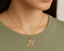 Gold necklace with a 'M' pendant/ charm worn by a person in a green shirt.