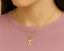 Gold necklace with a 'T' pendant/ charm on a person wearing a pink shirt