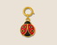 Gold ladybug charm with meenakari colours on a beige background