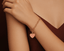 Gold bracelet with a gold pink heart charm on a wrist against a brown background